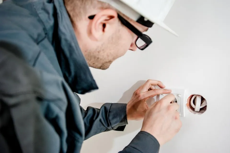 Electrician in a hard hat working on a wall outlet